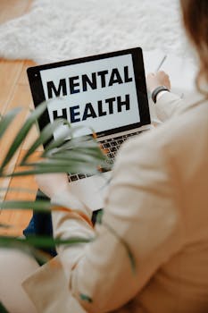 A woman focuses on mental health resources through her laptop in a home office setting.