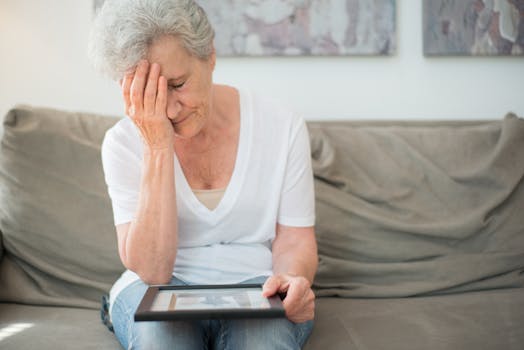 Thoughtful elderly woman on couch, holding a framed photo, deep in melancholy.